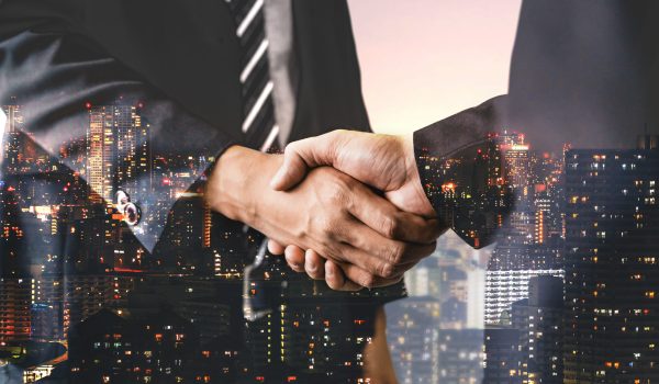 Double exposure image of business people handshake on city office building in background showing partnership success of business deal. Concept of corporate teamwork, trust partner and work agreement.